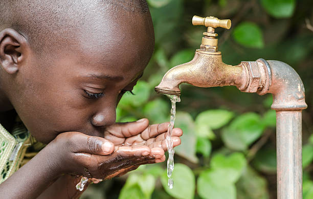 orgoglioso nero ragazzo e beve l'acqua da un rubinetto africa - foods and drinks simplicity purity clothing foto e immagini stock