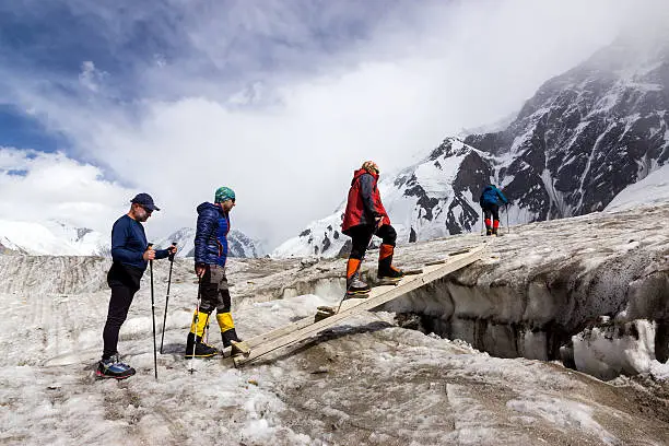 People Crossing Glacier Crevasse on Wood Shaky Footbridge Group of Mountain Climbers with High Altitude Boots and Clothing Crossing Ice Section During Ascent of Alpine Expedition in Asia Mountain Area