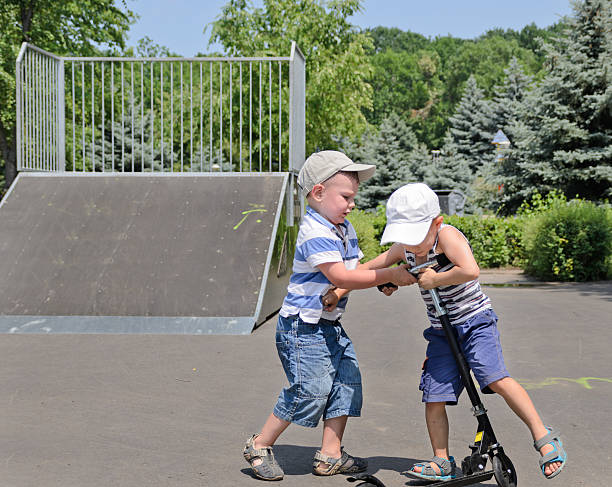 two young boys fighting over a scooter - låtsasbråk bildbanksfoton och bilder