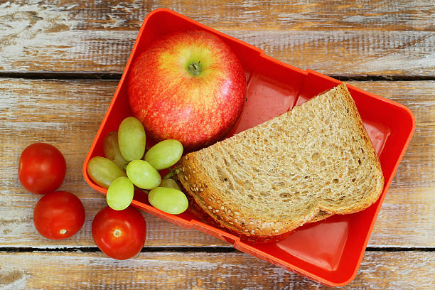 Lunch box with brown bread sandwich, apple, grapes and tomatoes