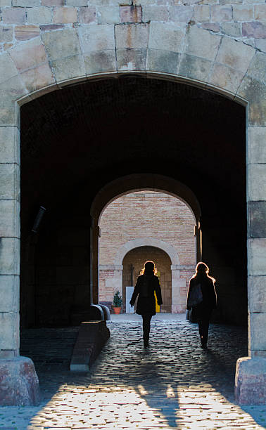 Backlighting Barcelona, Spain - January 30, 2014: Backlighting. Two young women walking backlit, inside the tunnel that gives access to the Castle of Montjuic, through its walls. tarde stock pictures, royalty-free photos & images