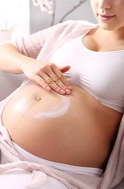 A pregnant woman rubs lotion on big pregnancy belly