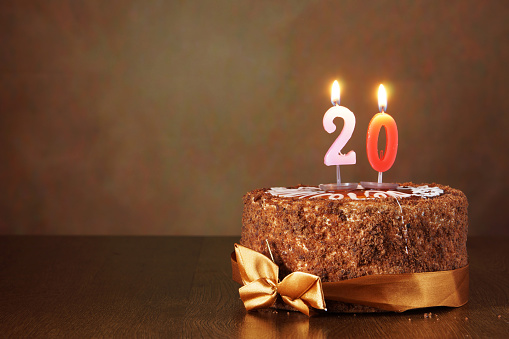 Birthday chocolate cake with burning candles as a number twenty on brown background