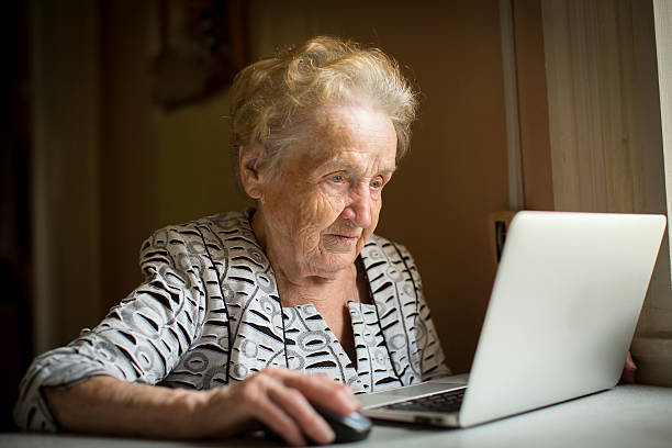 velha mulher sentada com laptop na mesa em sua casa. - grandmother action senior adult grandparent imagens e fotografias de stock