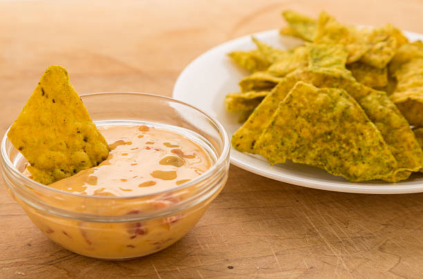 Cheese Dip with Jalapeno Tortilla Chips Dipping spicy jalapeno tortilla chips in creamy chili con queso dip in clear glass bowl. cheese dip stock pictures, royalty-free photos & images