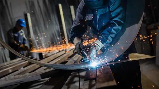 Man using welding torch to cut metal sheet in workshop.
