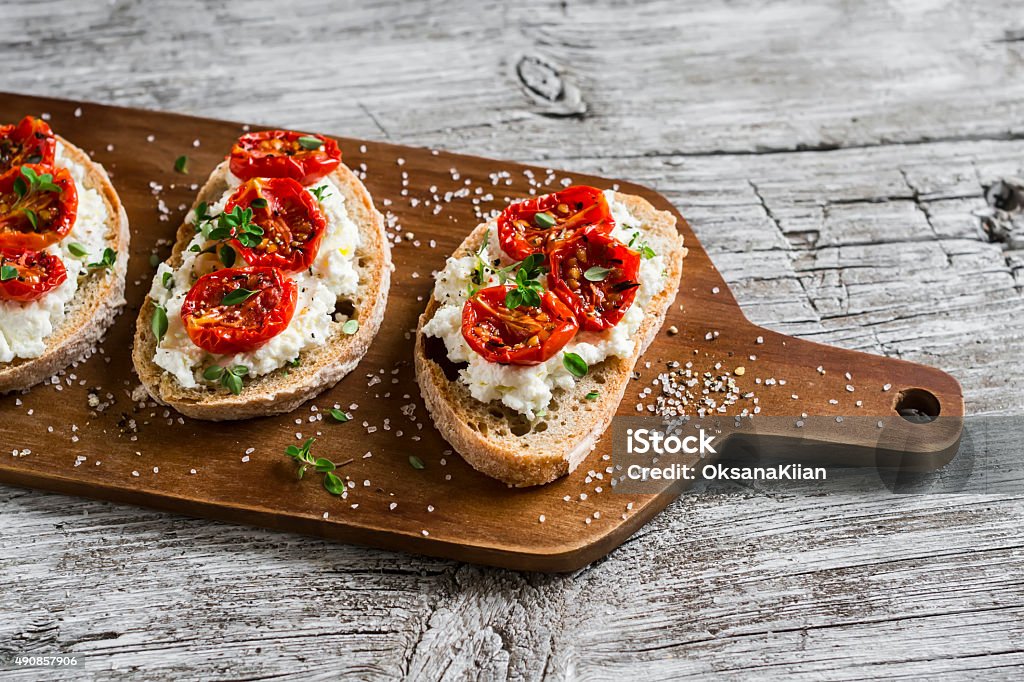 sandwich with goat cheese, sun-dried tomatoes and thyme sandwich with goat cheese, sun-dried tomatoes and thyme, served on the Board at a bright wooden surface Tomato Stock Photo