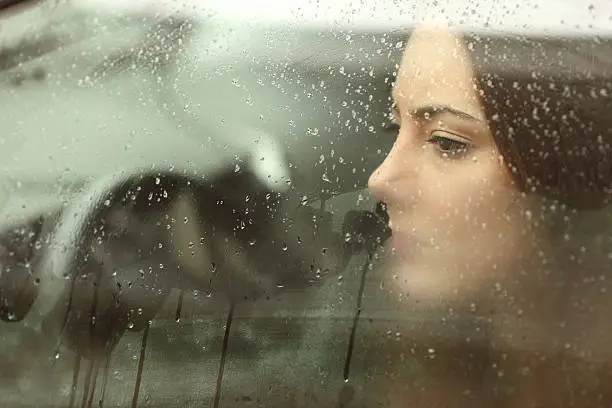 Sad woman or teenager girl looking through a steamy car window