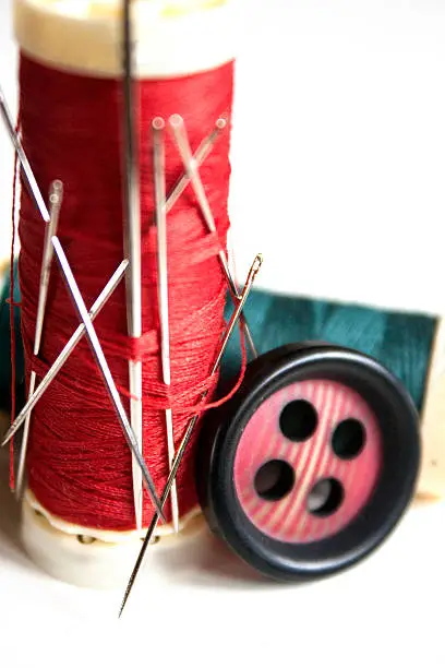 Red and grreen thread full of needles and sewing items on white background