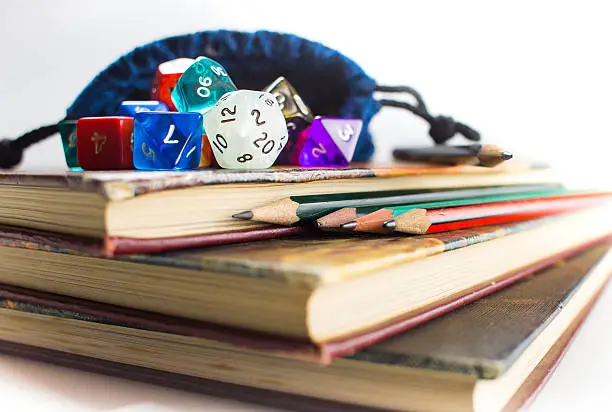 Close up of multicolored Dice with dice bag and Pencils on top of three Books