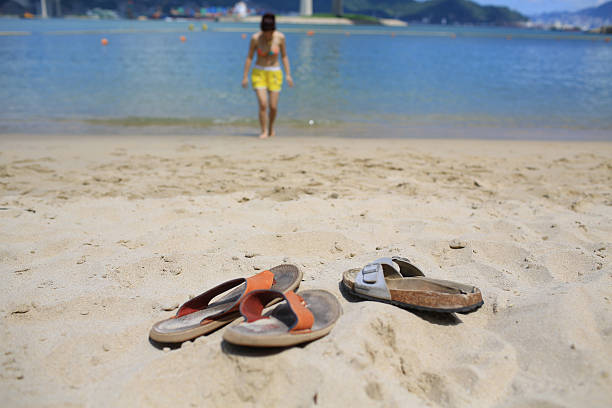 Top-down view of feet in flip-flops standing on sunlit beige beach sand with simple artistic drawings. Summer travel and vacation concept.