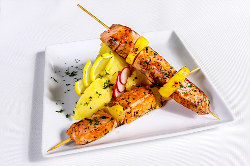 Two salmon skewers with potato garnish and lemons isolated on white background