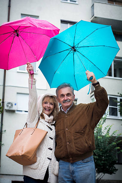 senior feliz casal na chuva com guarda-chuvas - umbrella senior adult couple autumn imagens e fotografias de stock