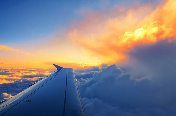 Wing of an airplane flying above the sunset clouds stock photo