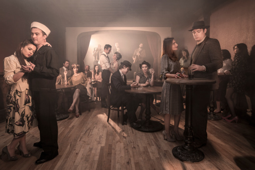Men and women in classy dress, with styles from a 1940s, post-Prohibition-era speakeasy.