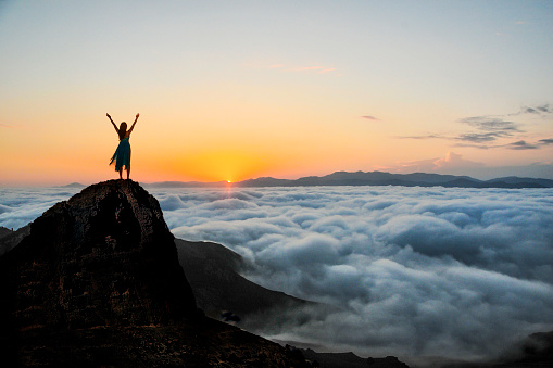 Woman enjoys on top of a cliff above the sea of clouds at sunset.