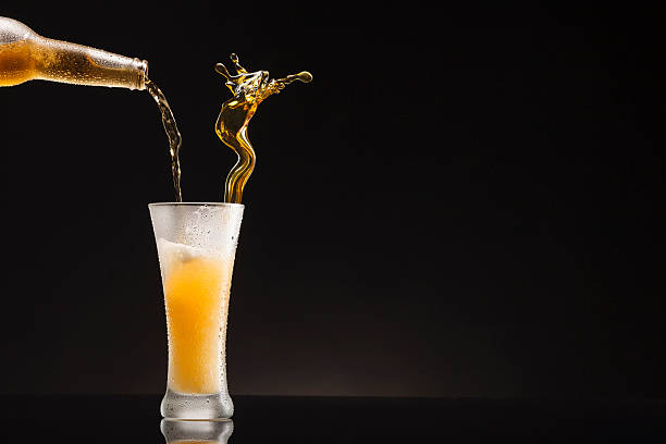 Ice cold Beer Pour from Bottle to Glass  with condensation Pouring beer splashing. Beer Pour from Bottle to Glass. Ice Cold Bottle and Mug of  Beer , covered with water drops - condensation. Glass standing on black table with black, dark gradient  background. beer glass splash stock pictures, royalty-free photos & images