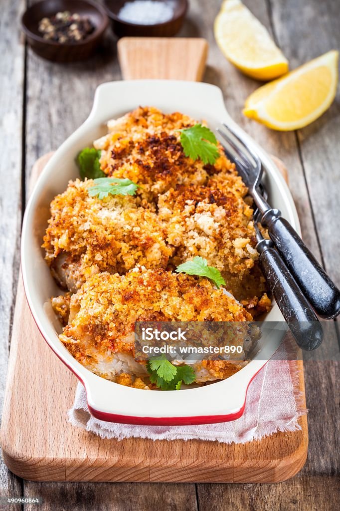 Baked cod fish in breadcrumbs in gratin dish Baked codfish in breadcrumbs in gratin dish on wooden table Pastry Dough Stock Photo