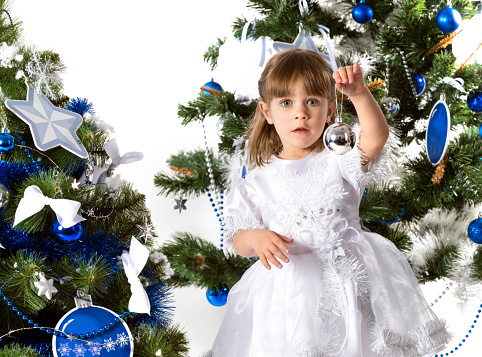 Girl dreams near the Christmas tree. Portrait of festively dressed girl, 3 years old.