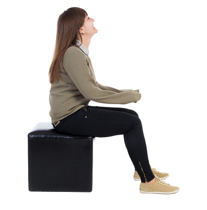 back view of young beautiful  woman sitting.  girl  watching. Rear view people collection.  backside view of person.  Isolated over white background. The girl is sitting on a leather ottoman and smiling.