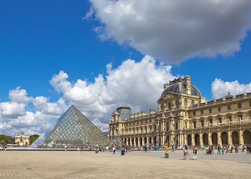 Paris, France - July 30, 2015: View of Pyramid at courtyard of Louvre Museum with tourists sightseeing and making pictures with Triumph Arch on the background