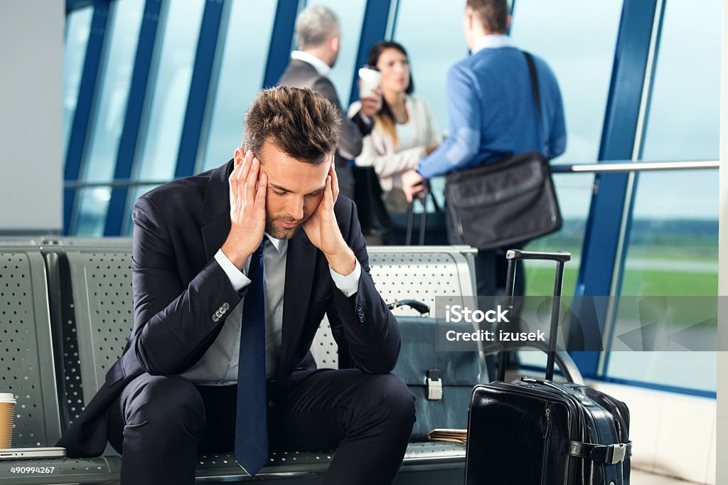At the airport Businessman waiting for a flight at the airport lounge, sitting tired on a banch, group of people standing in the background. Jet Lag Stock Photo