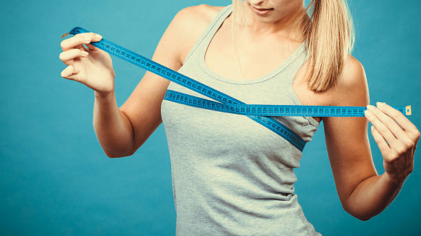 Fitness girl measuring her breasts Fitness woman fit girl in sportswear with measure tape measuring her size chest breast on blue bra stock pictures, royalty-free photos & images
