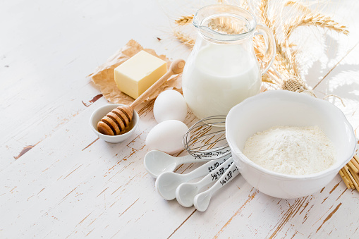Baking ingredients - milk flour butter eggs, white wood background, copy space