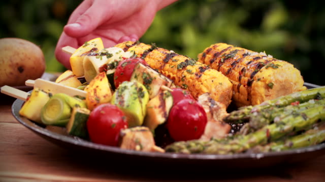 Person taking a delicious grilled vegetable kebab from plate outdoors