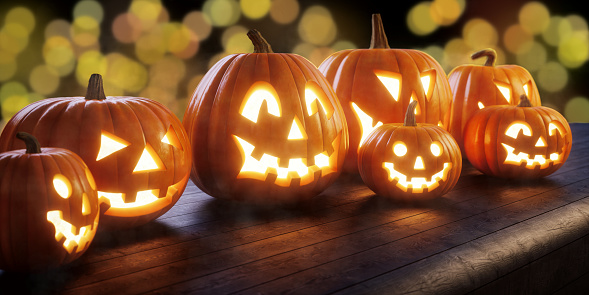 A family of Jack O' lanterns sitting on a dark wooden bench, with bokeh lights in the background.