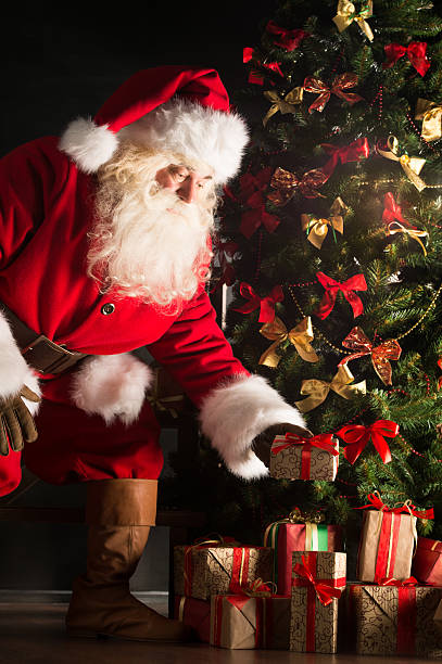 istock Santa putting gifts under Christmas tree in dark room 491056400