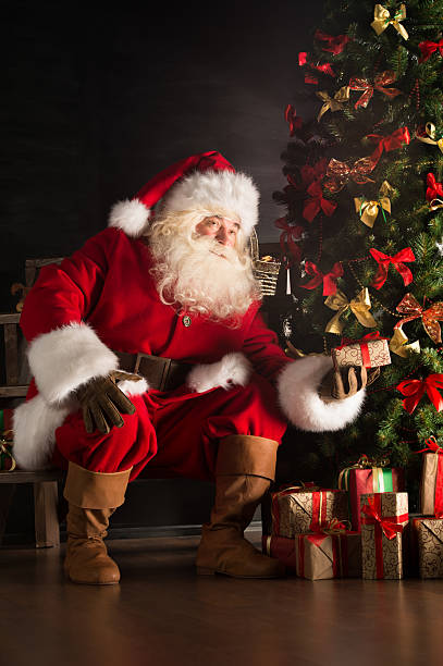 istock Santa putting gifts under Christmas tree in dark room 491056426