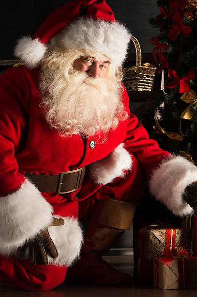 istock Santa placing gifts under Christmas tree in dark room 491057294