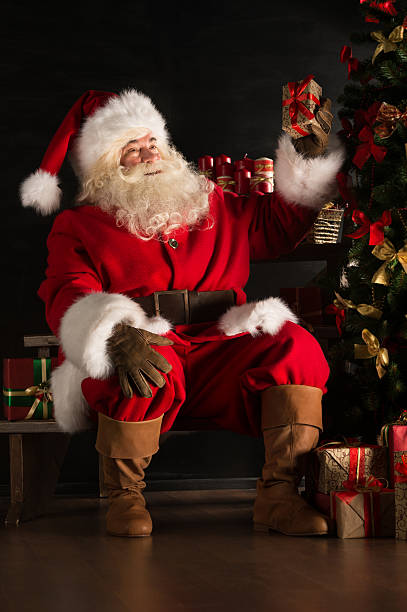 istock Santa placing gifts under Christmas tree in dark room 491057314