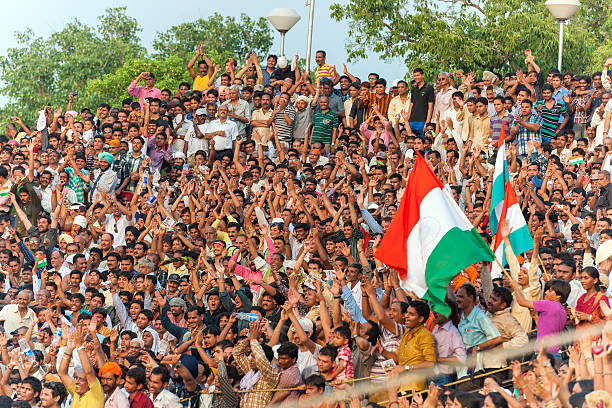 Wagah, India - July 10, 2011: Crowd on the Indian side standing on the stand and shouting patriotic words before and during the Lowering of the Flags, India-Pakistan border, hot summer day; Punjab, India.Some of the people are holding big Indian flags.