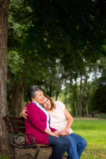 A elderly mother and daughter hugging each other in the park.