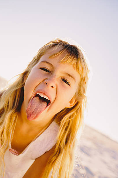 A little girl with blonde hair, in her swimmers, eating sand at the beach