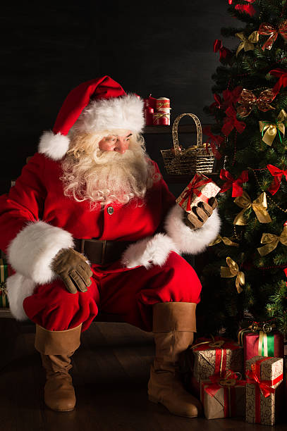 istock Santa putting gifts under Christmas tree in dark room 491069780