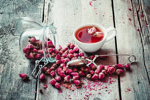 Dry rose buds, tea cup, strainer and glass jar with rosebuds. Selective focus.