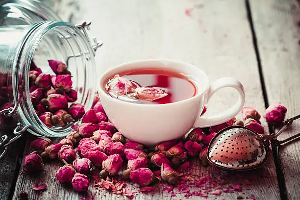 Rose buds tea, tea cup, infuser and glass jar with rosebuds. Selective focus.