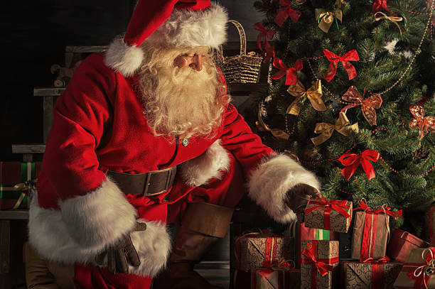 санта помещает подарочные коробки под christmas tree - santa claus стоковые фото и изображения