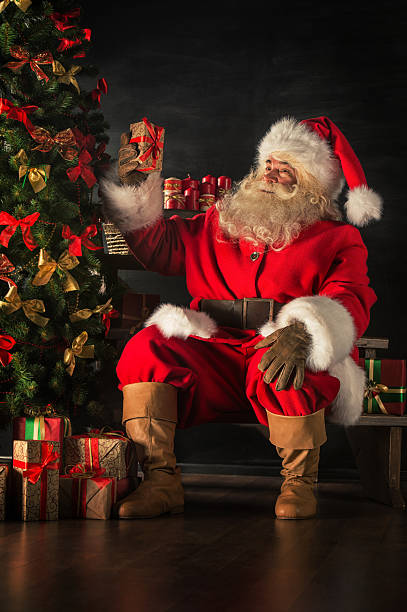 Santa is placing gift boxes under Christmas tree stock photo