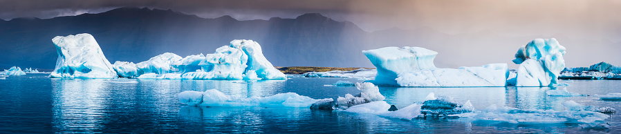 Electric blue icebergs calved from the Vatnajökull ice cap reflecting in the tranquil ocean lagoon of Jokulsarlon beneath dramatic Arctic skies in Iceland. ProPhoto RGB profile for maximum color fidelity and gamut.