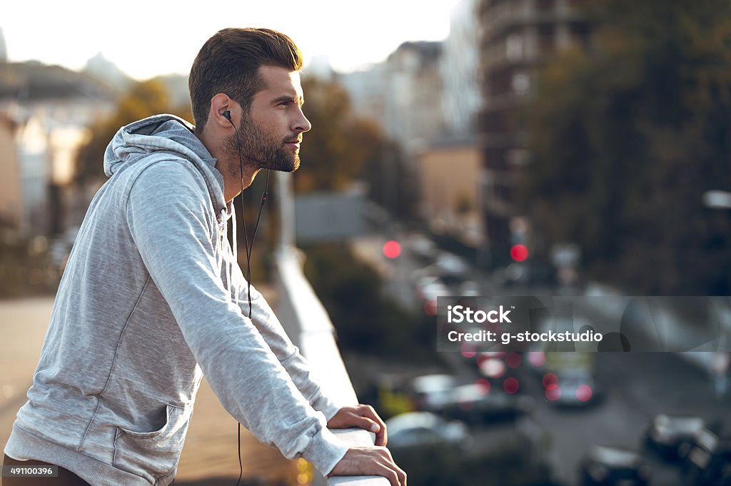 In love with his city. Side view of pensive young man in headphones looking away while standing on the bridge 2015 Stock Photo