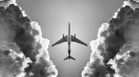 Black and White picture of the airplane fly between the black cloud.