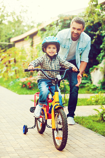 Happy little boy riding bicycle and smiling while father helping him