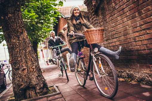 Young woman enjoys bicycle ride in the city, followed by her male partner, also on bike 