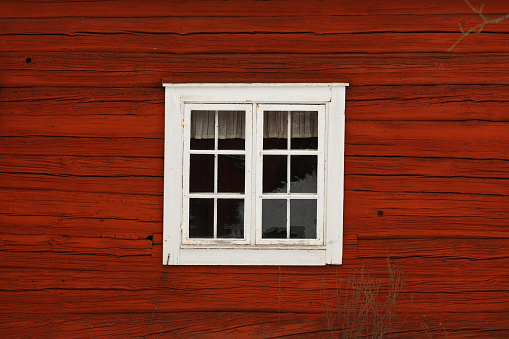 White window on an old-fashioned cottage painted in swedish traditional red color.