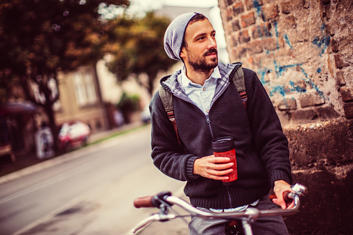 Young man enjoys bicycle ride in the city along side with a cup of coffee to go