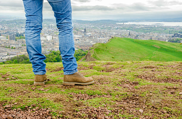 Focus on legs of a female model in skinny jeans Focus on legs of a female model wearing skinny blue jeans and brown suede boots admiring Edinburgh landscape from the top of the Arthur's seat. Scotland, UK. womens blue suede shoes stock pictures, royalty-free photos & images